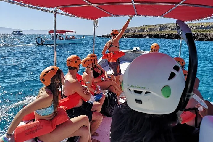 Turistas con chalecos salvavidas y cascos naranjas sentados en una lancha bajo un toldo rojo, navegando por aguas azules cristalinas en Bahía de Banderas.