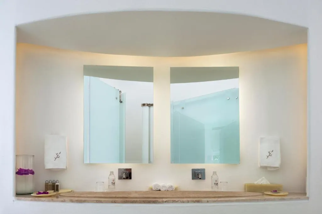 Baño de hotel de lujo con dos espejos iluminados, toallas blancas y decoración minimalista.